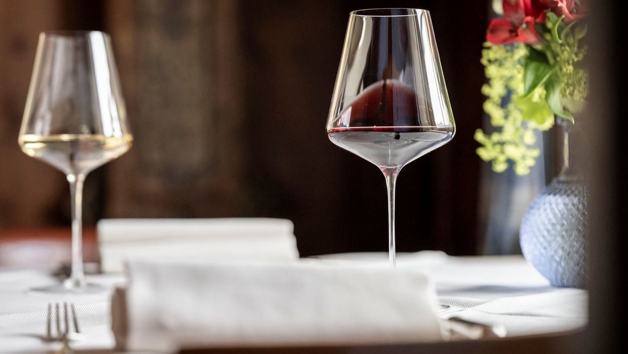 Two wine glasses, one with white wine and one with red, on a table in an old tavern, next to a vase of flowers.