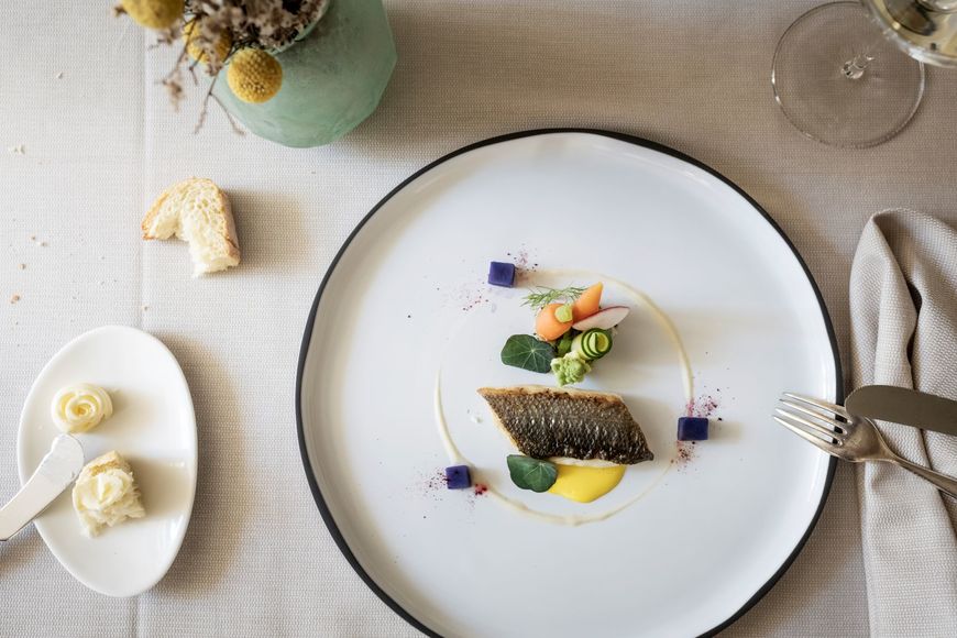 Fish dish with butter, bread, wine glass, and flower vase on an elegantly set table. ©Löwengrube/Alex Filz