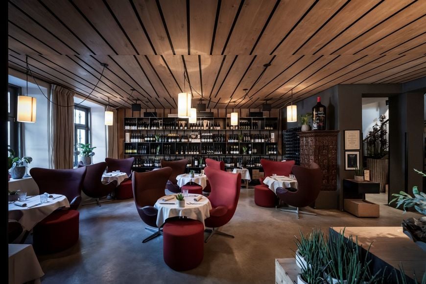 Interior of the restaurant with set tables, cozy armchairs, and a large wine display in the background. ©Löwengrube/Alex Filz