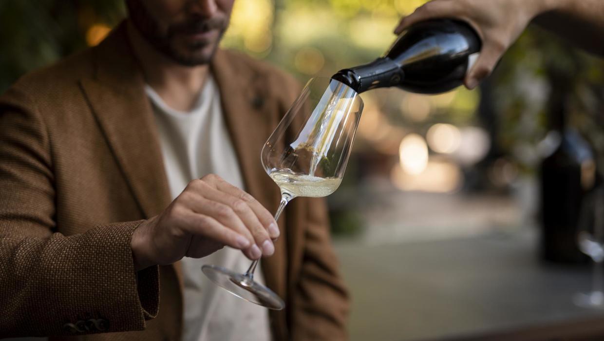 A man being poured a glass of white wine.